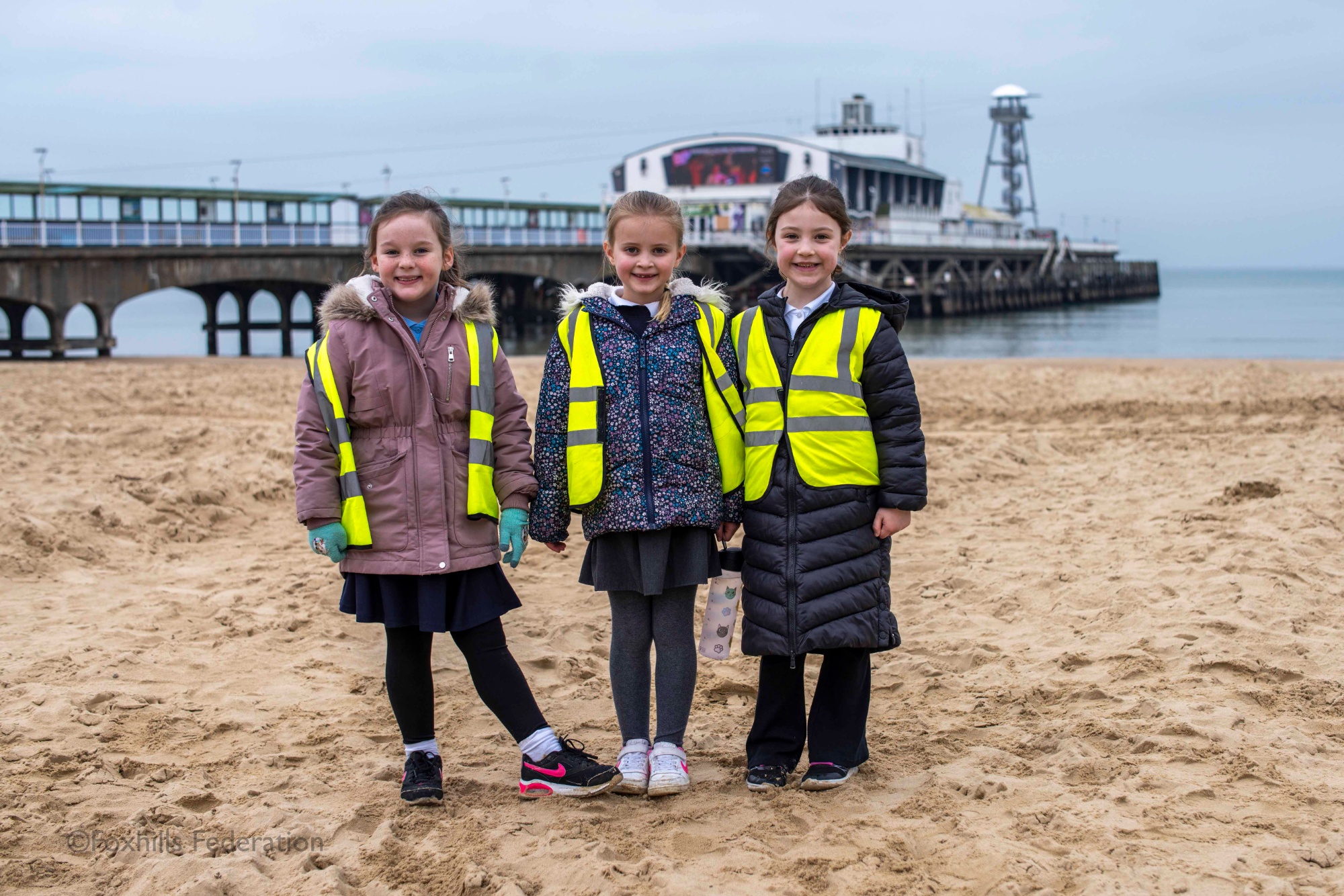 A group of children smile and pose in front of Bournemouth pier.