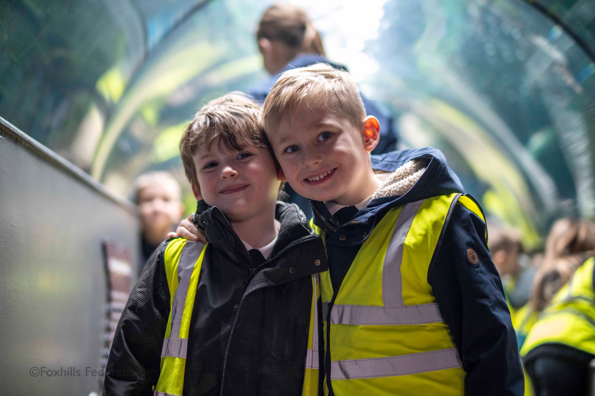 Two boys smile at the camera in a glass tube.