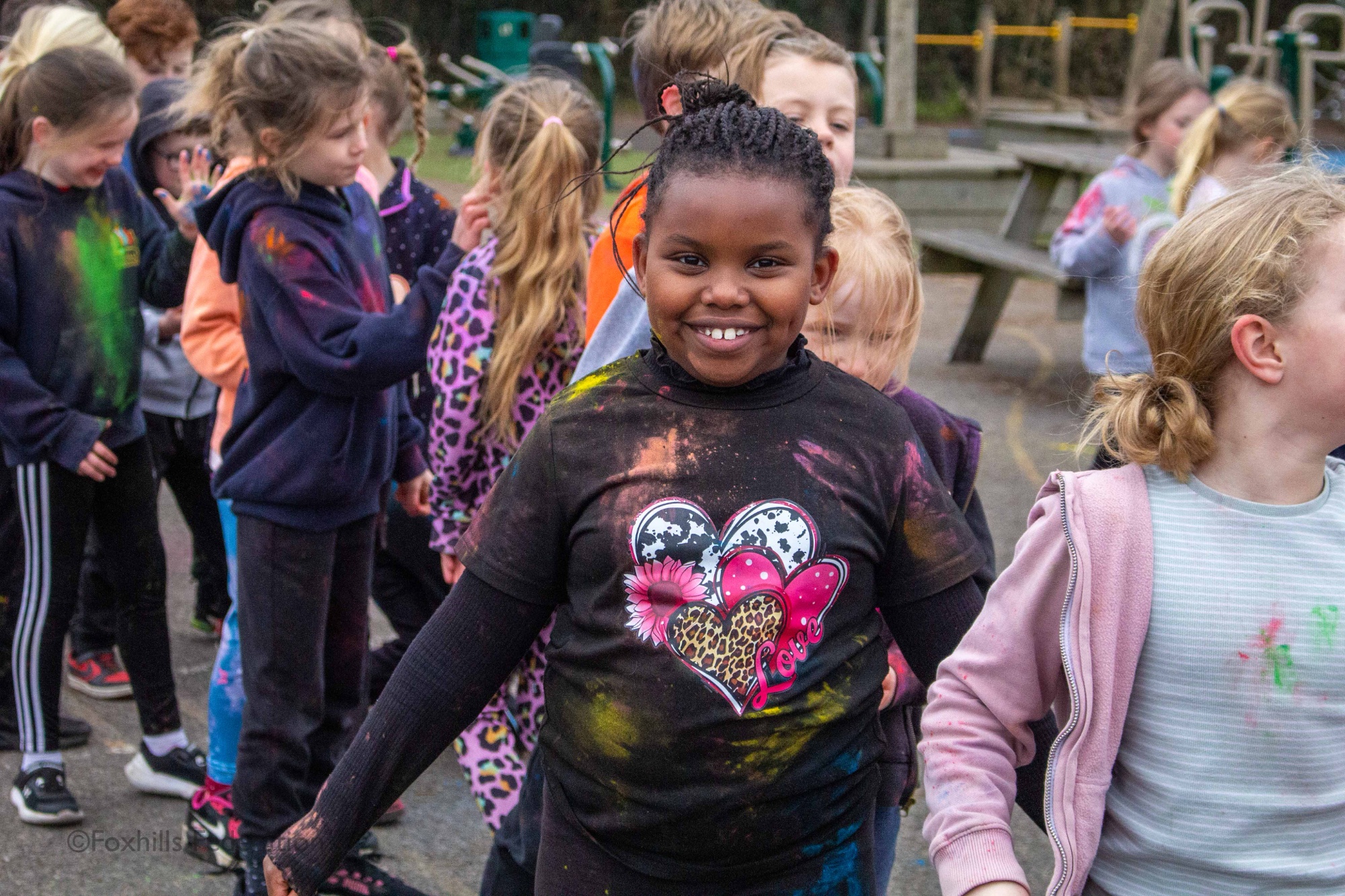 A year 3 girl smiles while covered in brightly coloured paint